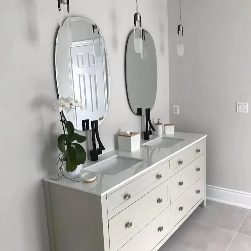 A white double vanity with two round mirrors and black faucets.