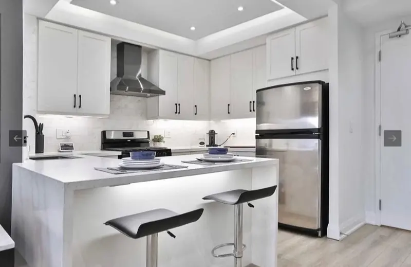 A white condo kitchen with an island, bar stools and stainless appliances.