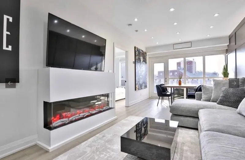 A condo living room with a long electric fireplace under a wall-mounted TV and city views.