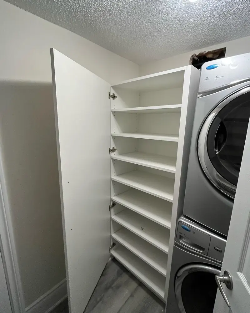 A tall white storage cabinet beside a stacked washer and dryer.