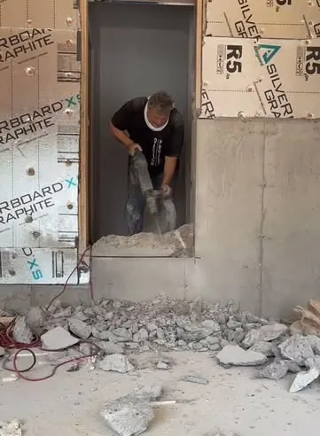 A worker breaking up concrete with a jackhammer in a basement doorway.