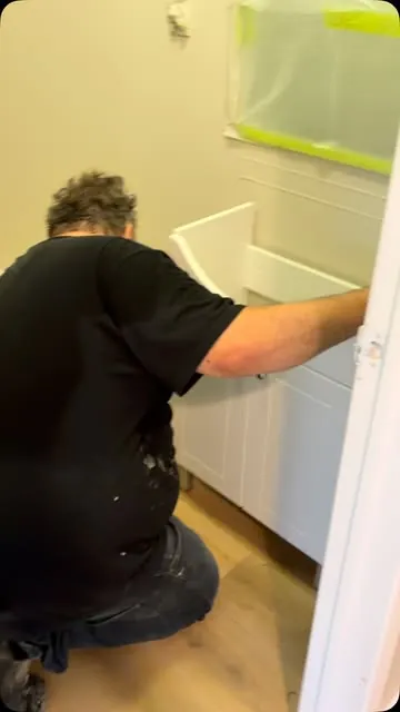 A DPC installer kneeling to fit a white bathroom vanity.